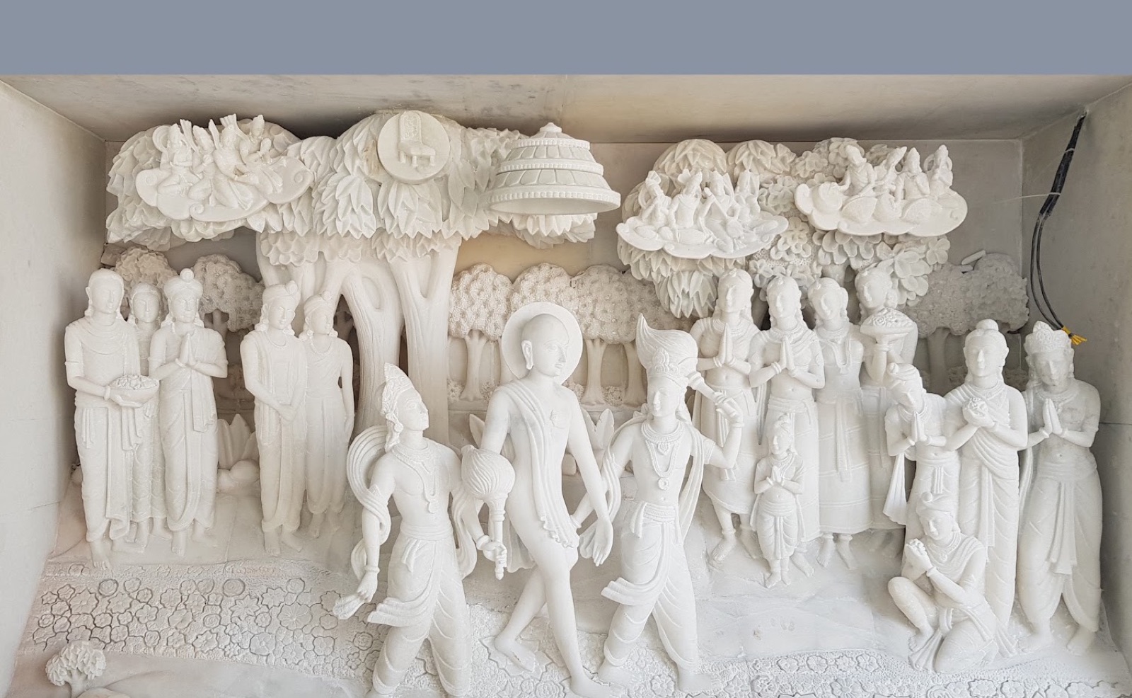 White marble relief of a procession of figures beneath carved trees