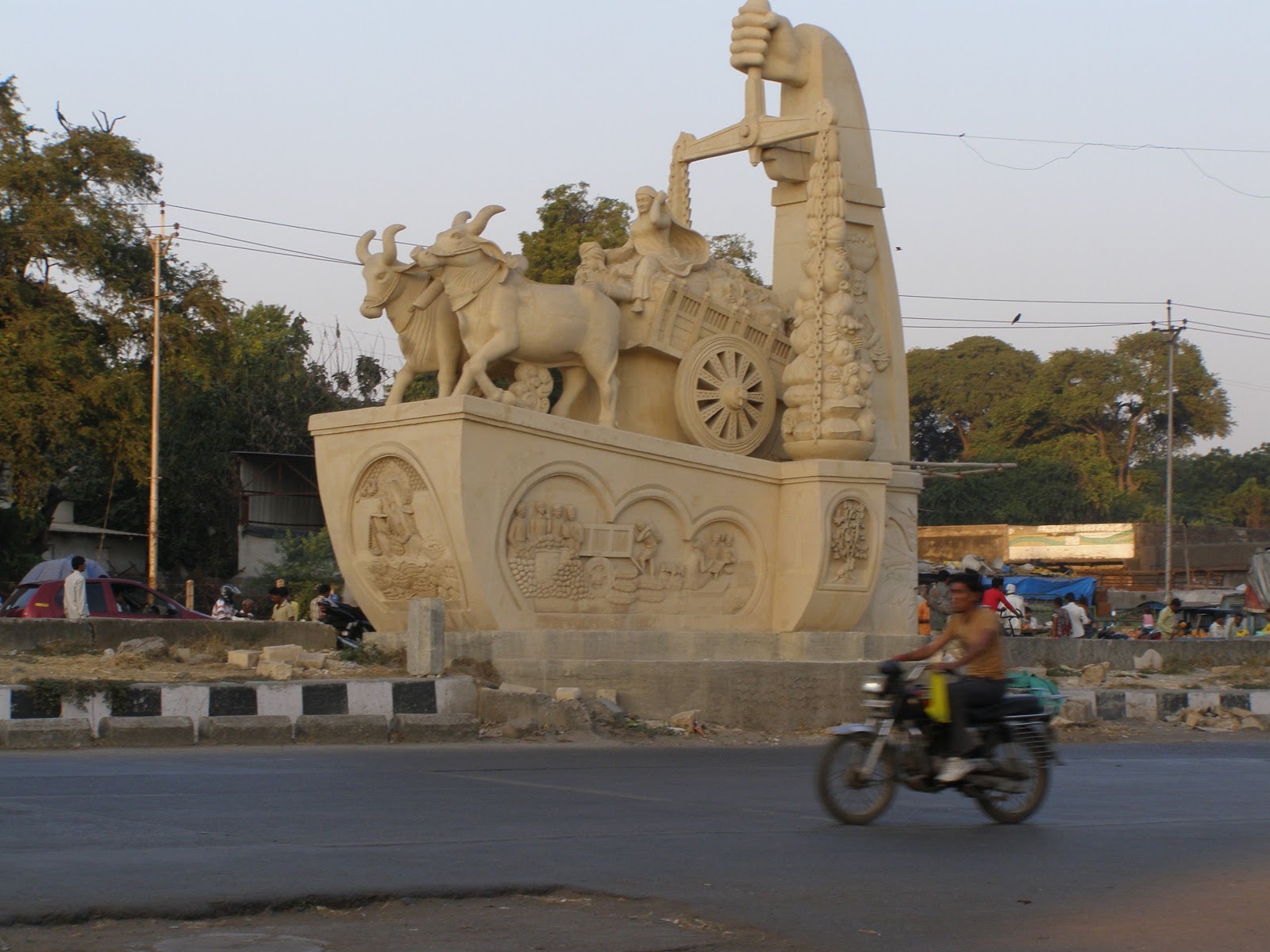 Sandstone traffic-circle monument of a bullock cart on a relief-carved plinth