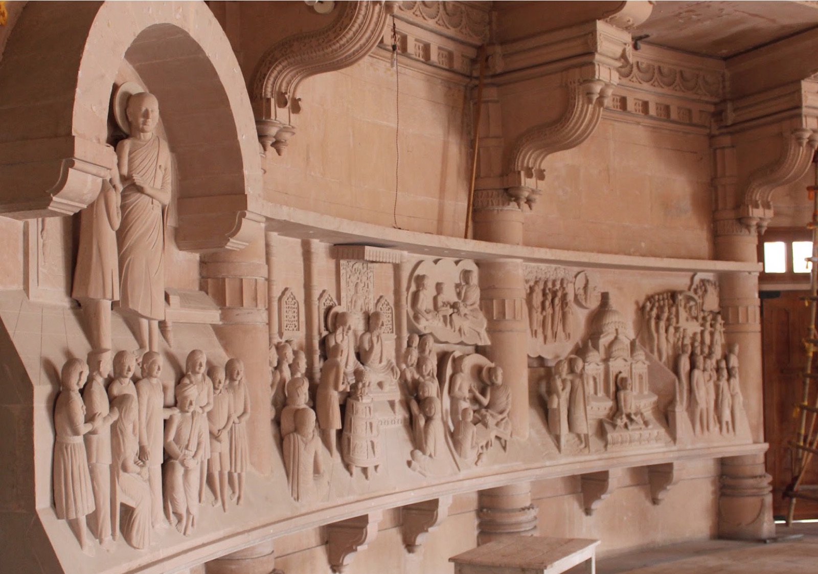 Sandstone wall frieze of carved narrative scenes below an arched niche with a standing figure